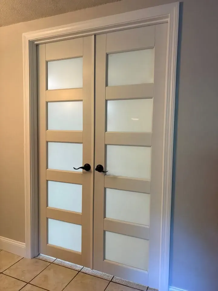 Close view of new double French doors with frosted glass lites, trimmed out and painted white, in a hallway with grey-blue walls.