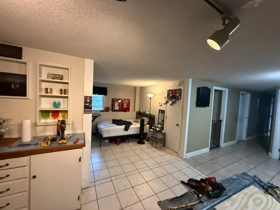 A basement room mid-job, looking through to a bedroom area, with tools and a table saw on the tile floor.