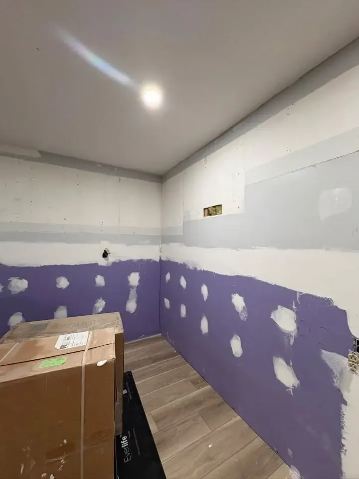 A small room with new drywall, purple moisture-resistant board along the lower wall with screw spots mudded, and plank flooring.