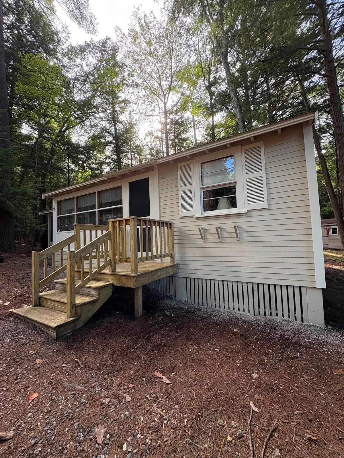 A cottage with beige vinyl siding and white shutters, and a new pressure-treated deck landing with stairs and railings.