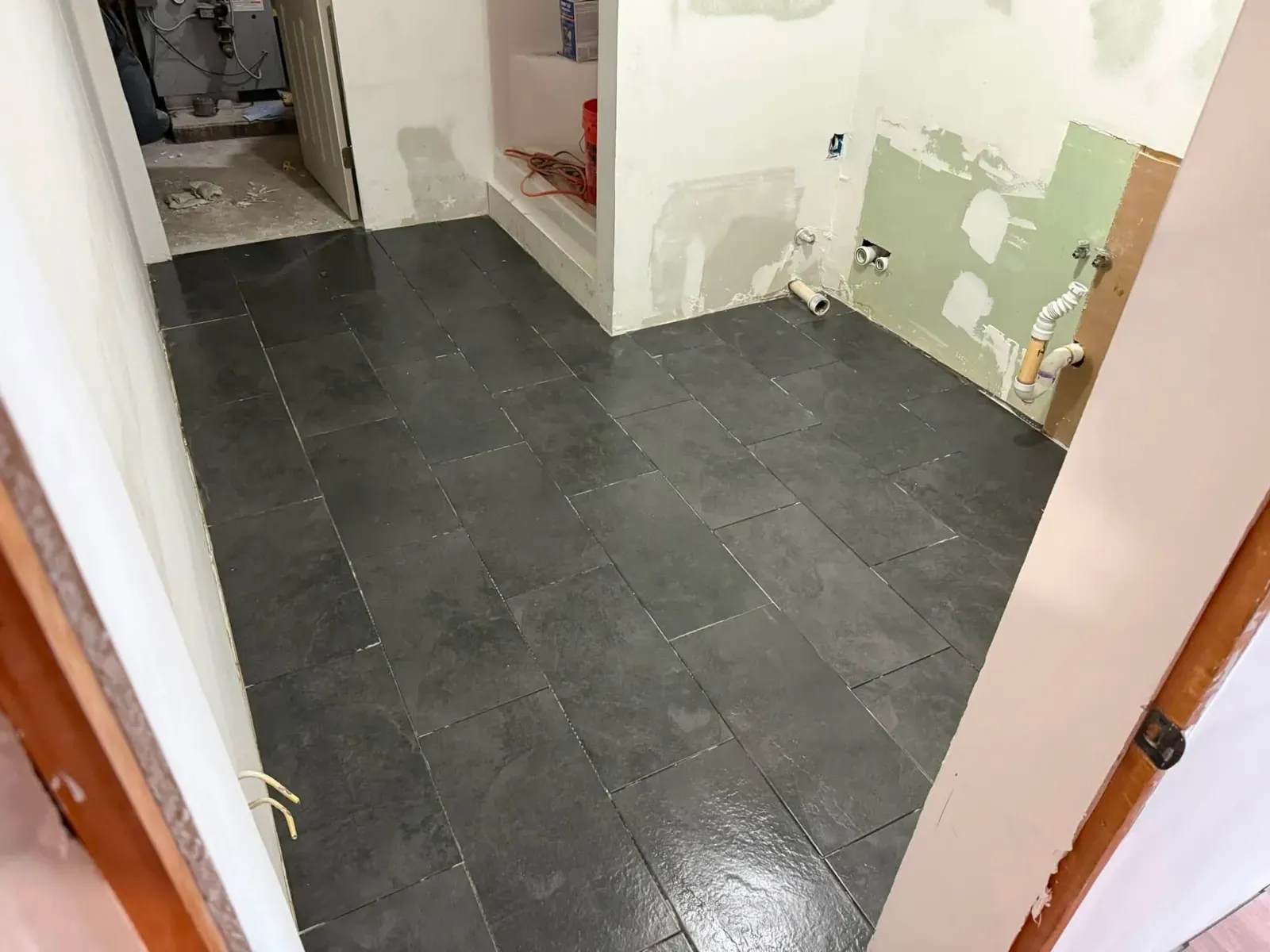 A dark slate-look tile floor in a small room with the walls stripped and patched, mid-renovation.