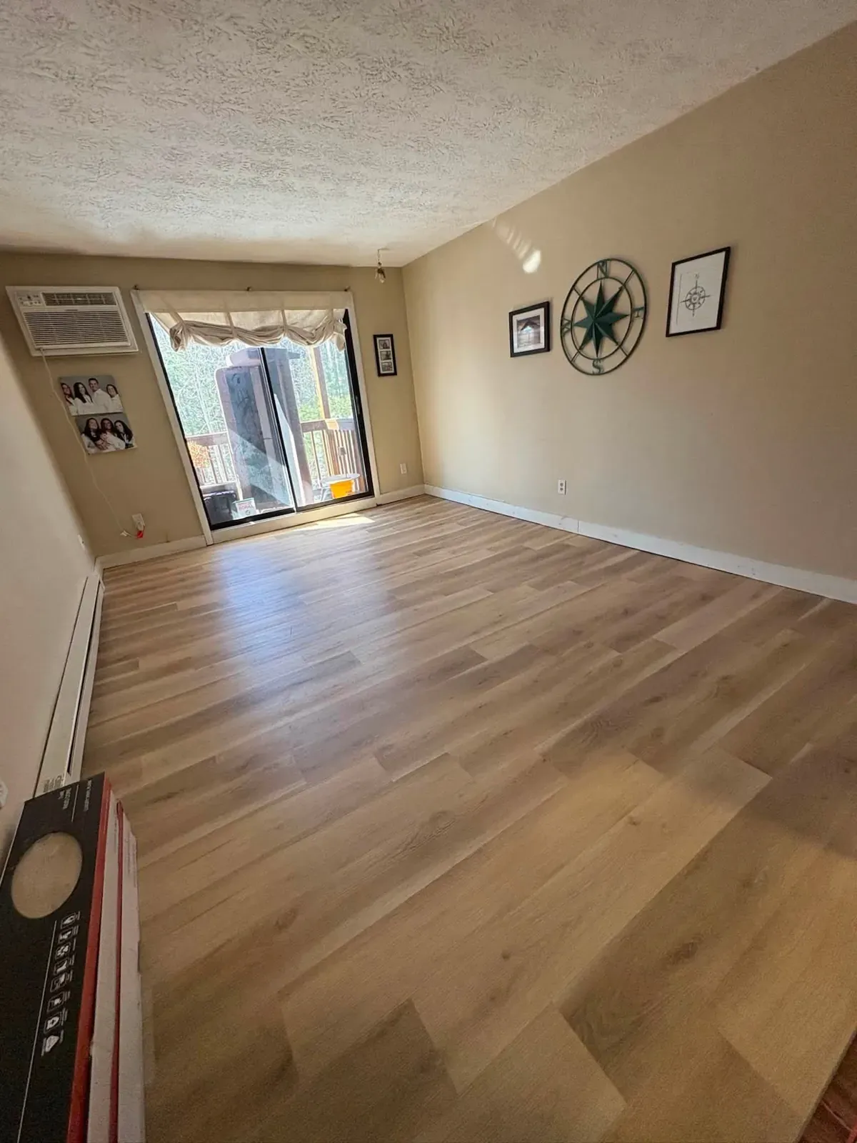 A long living room with new warm oak-look plank flooring leading to a sliding door, and a compass wall hanging.