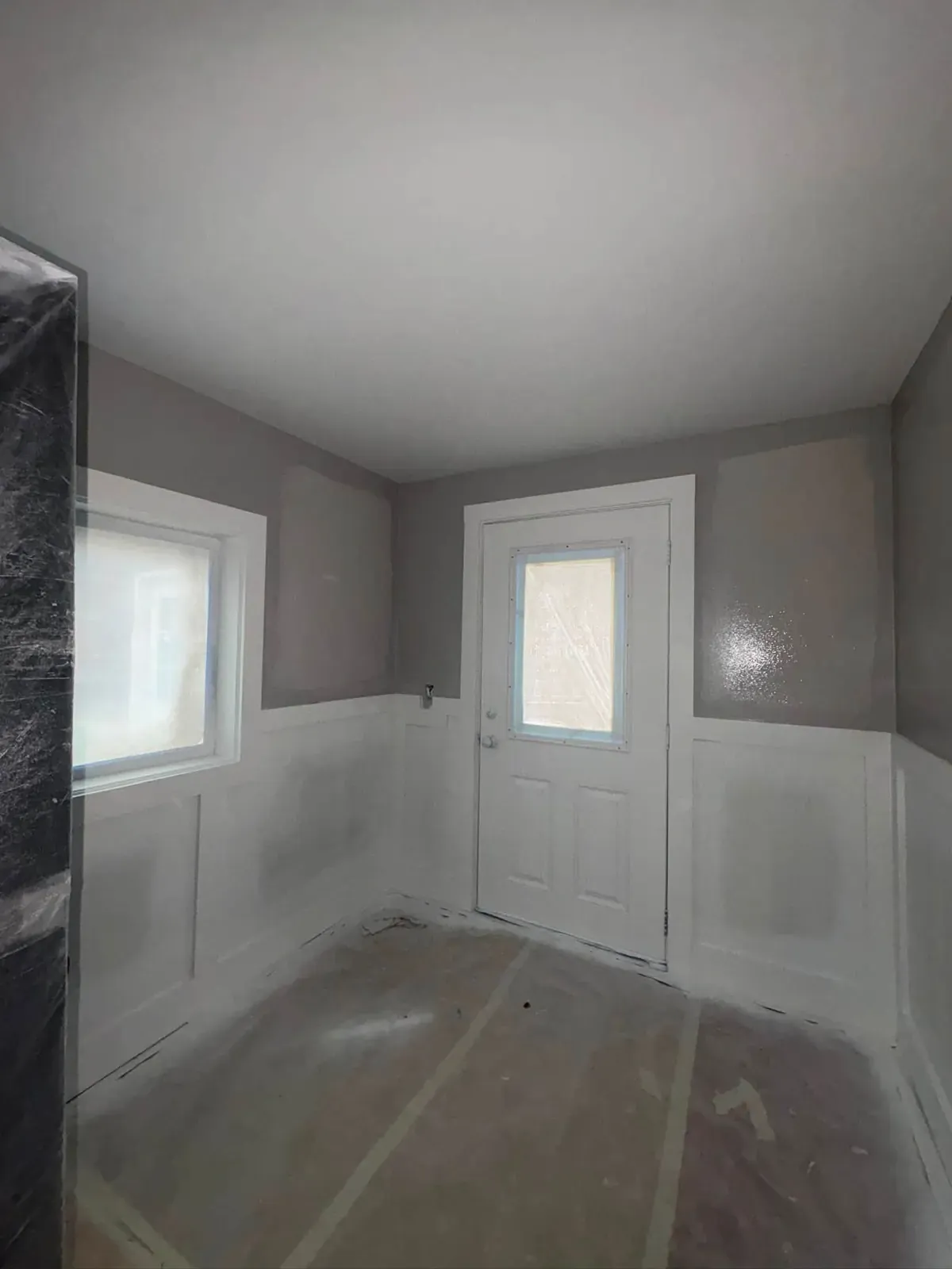 A small entry with new white wainscoting panels on grey walls and a white door with a half-lite window.