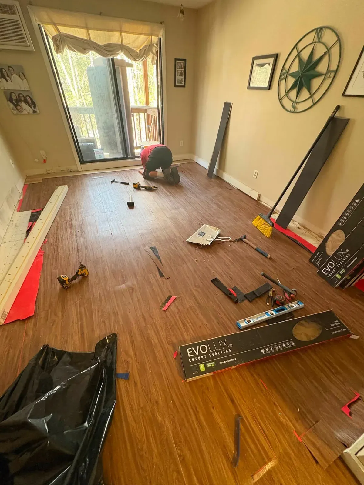 Luxury vinyl plank flooring being installed across a room, with boxes of planks, cut offcuts and tools on the floor.