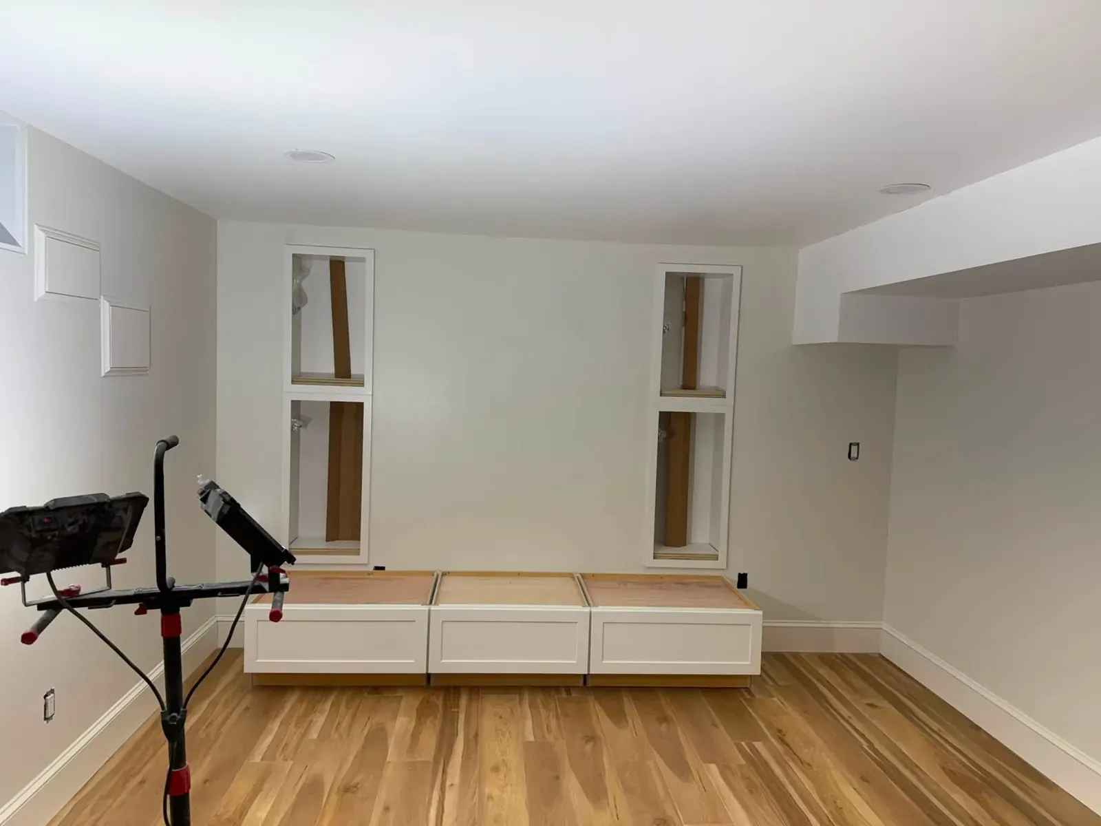 A bright white basement room with new honey-oak plank flooring and a low built-in bench along one wall.