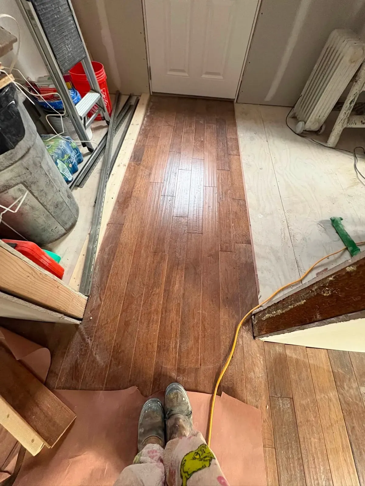 A narrow dark hardwood-look floor being run down a hallway, with tools, a radiator and a paper floor cover alongside.