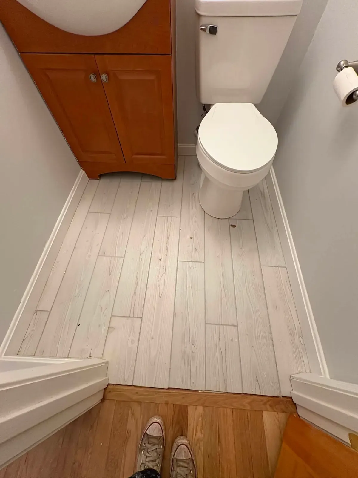 A half bath with new whitewashed plank flooring, white baseboard, a toilet and a wood vanity, seen from the doorway.