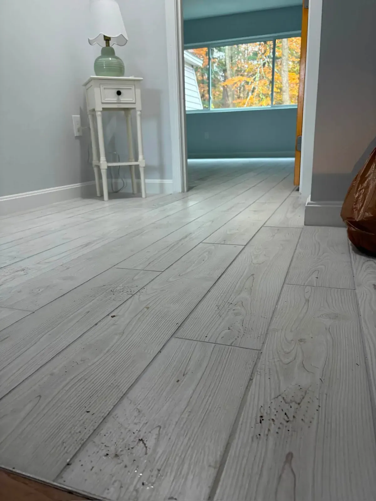 A bedroom with new pale grey weathered plank flooring and a small white side table by a window.