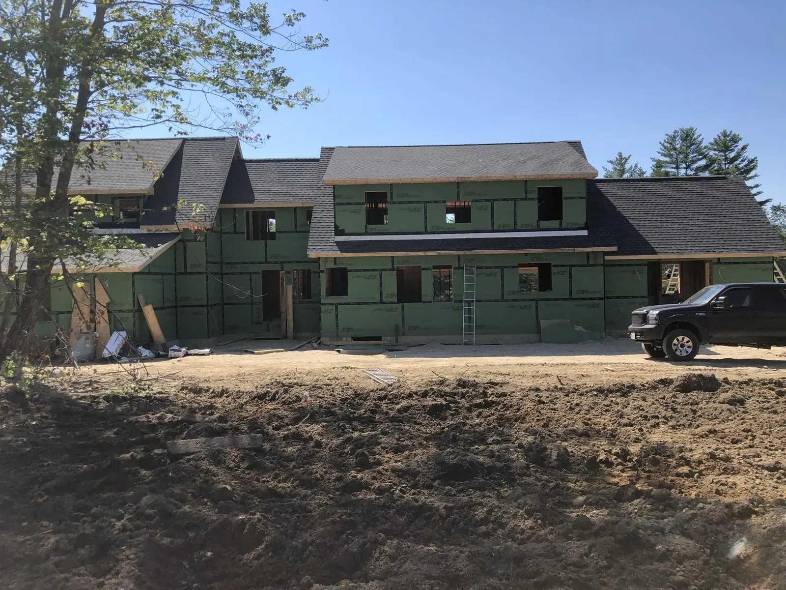 A new two-story house under construction, framed and sheathed with green wall wrap, a pickup truck parked beside it.